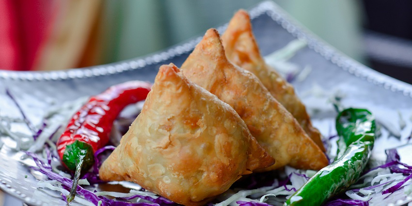 An image of Samosas, the best street food in India, garnished with cilantro and a drizzle of sauce, placed on a woven mat