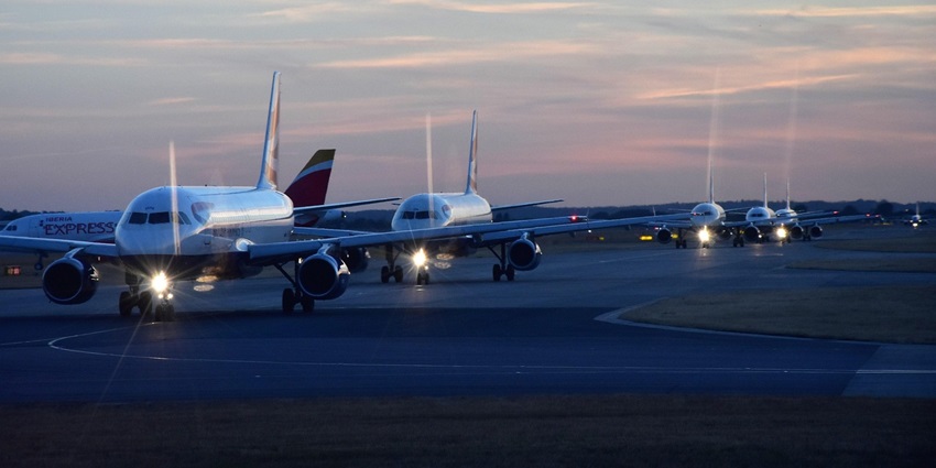 A couple of aeroplanes wait in the hangar where the pathway is blue and the sky is pinkish