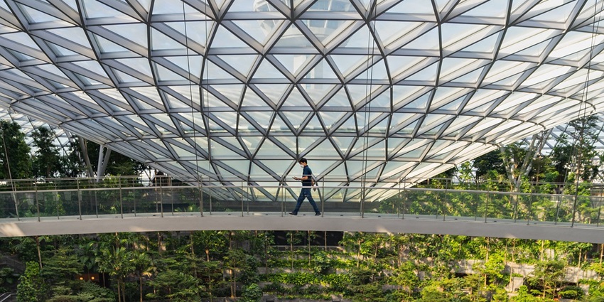 Inside of an airport with glass ceilings and green plants bordering, a man walking by