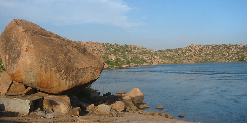 Sanapur Lake in Hampi, with lush greenery and rocky hills surrounding the calm water.