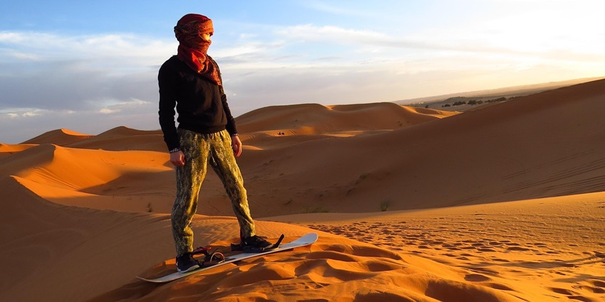 Image of a person sandboarding on the golden dunes of the Sahara Desert at sunset