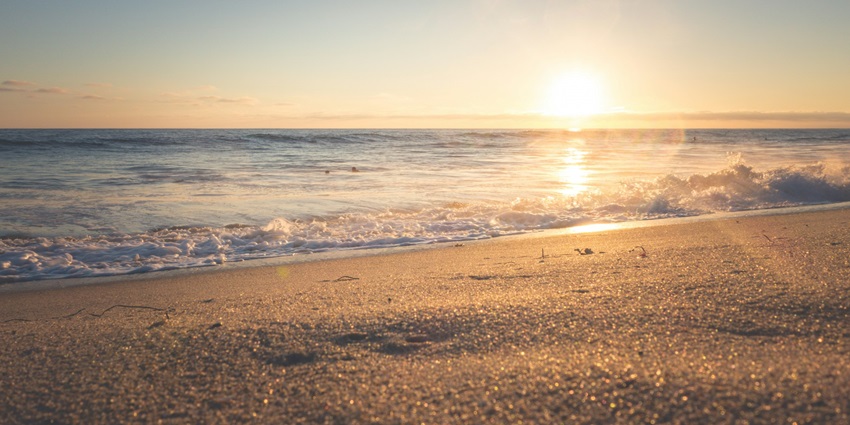 Sunset over a peaceful seashore with gentle waves and golden light on the water