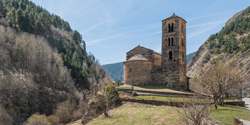 Saint Joan de Caselles surrounded by hills and trees in different shades, with a blue sky above