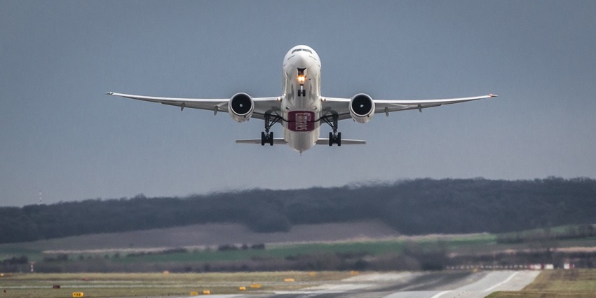 A plane has just taken off from the ground and is in the air with one of its lights