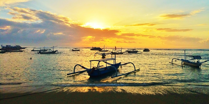 A peaceful sunrise view at Sanur Beach with traditional Balinese boats on the shore.
