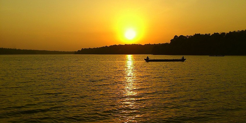 Sasthamcotta Lake with a large water body, silhouette of men boating and the sun setting