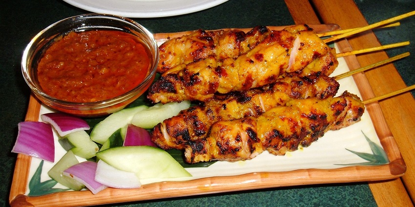 An image of the grilled skewered meat served with rich peanut sauce and fresh vegetables