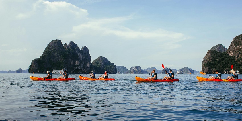 Groups of people kayaking on calm blue water surrounded by rocky islands under clear skies