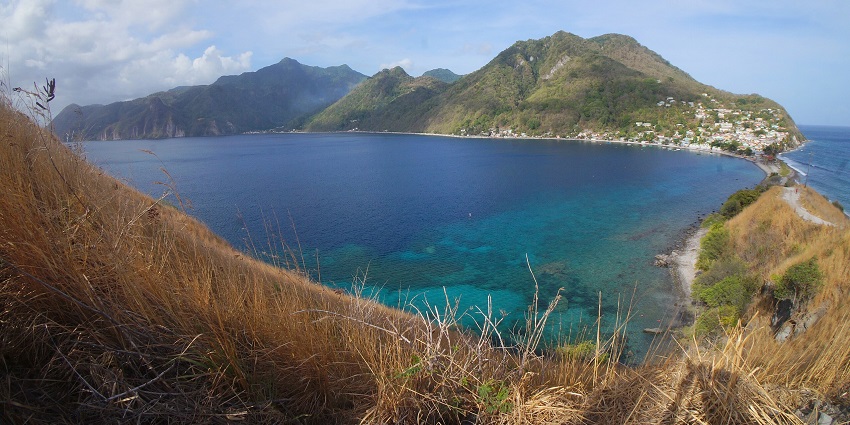 Panoramic view of the full Scotts Head village, showing a green landmass and blue waters