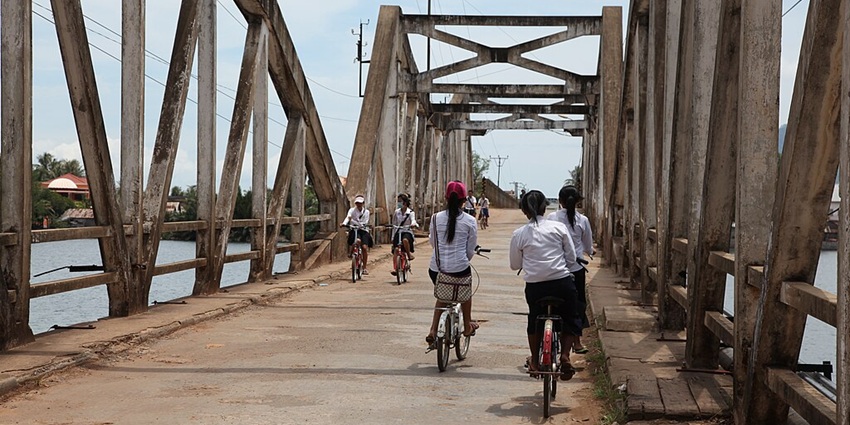 An image of a group of people cycling on the Old Bridge in Kampot, Cambodia.