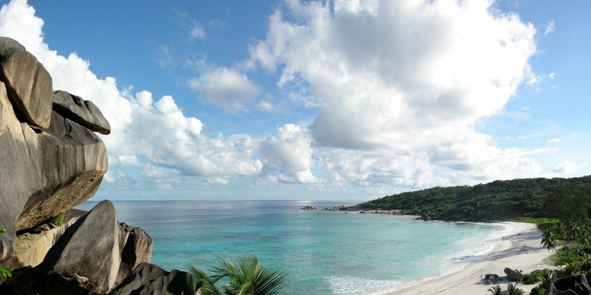 An image of Grand Anse beach with large granite boulders, white sand, and clear water