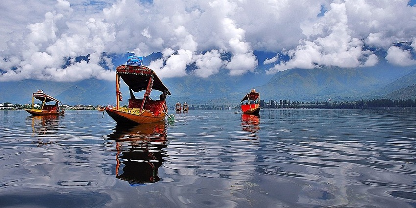 Shikara ride boats in Dal Lake with a large water body and mountains covered in clouds