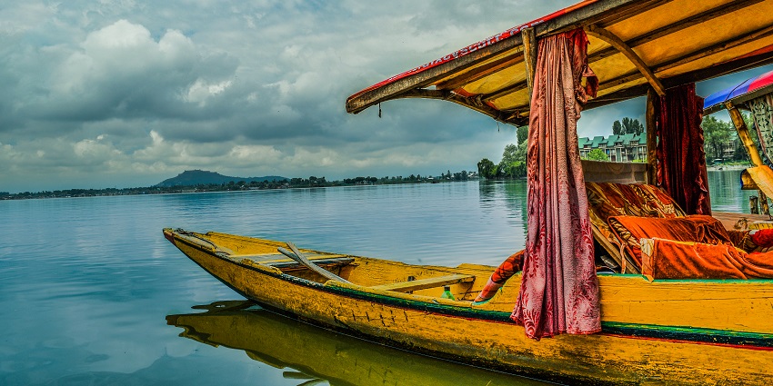 Shikara boat on a lake with yellow wooden build, curtains, mountains under a clouded sky