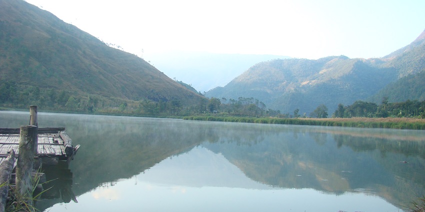 Shilloi Lake is surrounded by green hills, with calm waters reflecting the dense vegetation