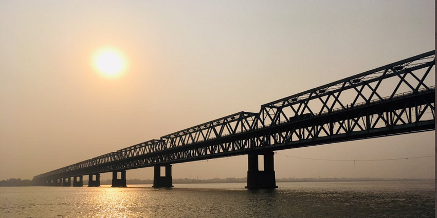 Multiple people at the stairs of Simaria Ghat leading to the river and a bridge over it