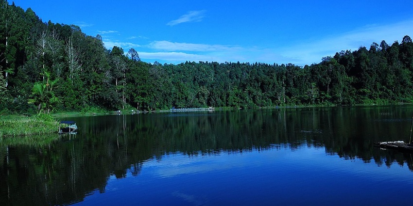 A serene lake scene at Situ Cibeureum, reflecting lush green forests and misty mountain peaks in the tranquil water.