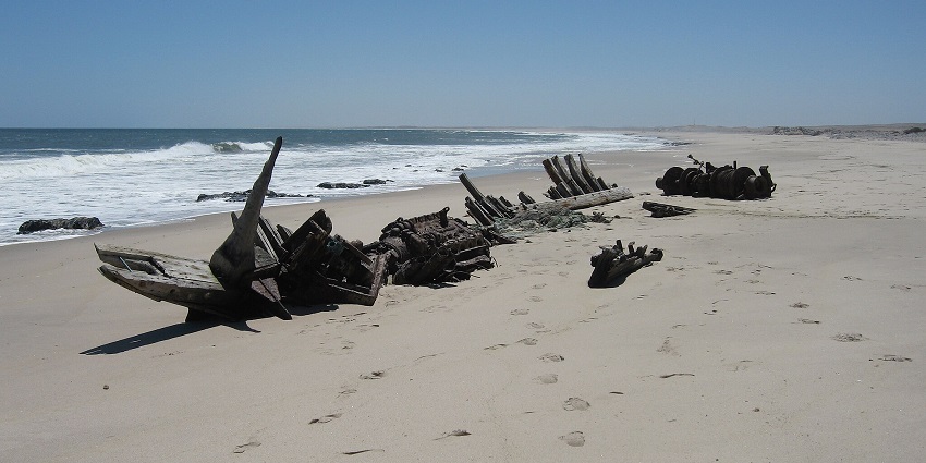 Shipwreck remains on Skeleton Coast, one of the famous beaches in Africa, with waves crashing against the rusted frame.
