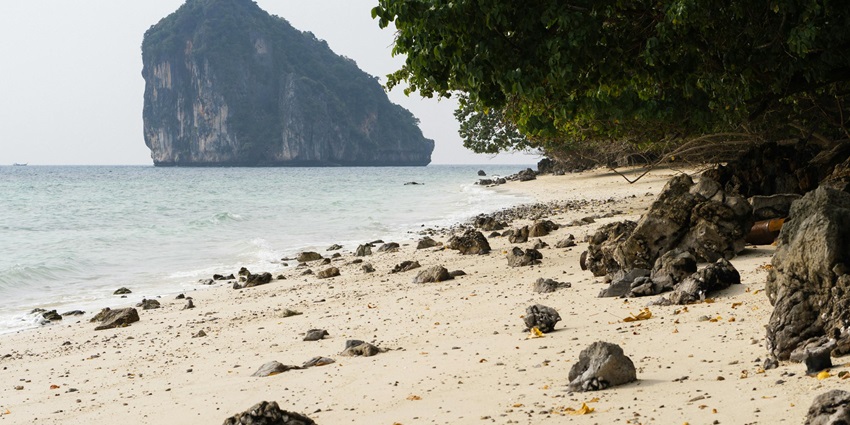 Several small stones and rocks on the sandy shores of a beach with a limestone cliff