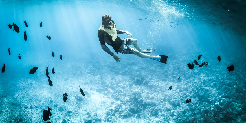 An image of snorkelling in clear turquoise water, wearing a red and black life jacket.