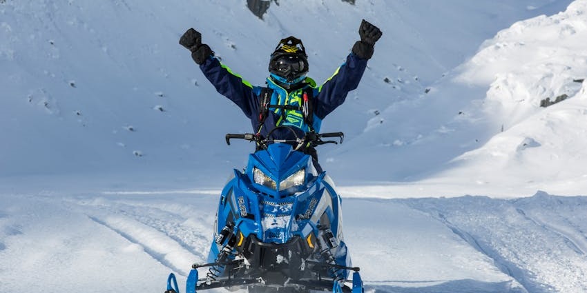 Person raising hand while sitting on a blue snowmobile with white snow all around