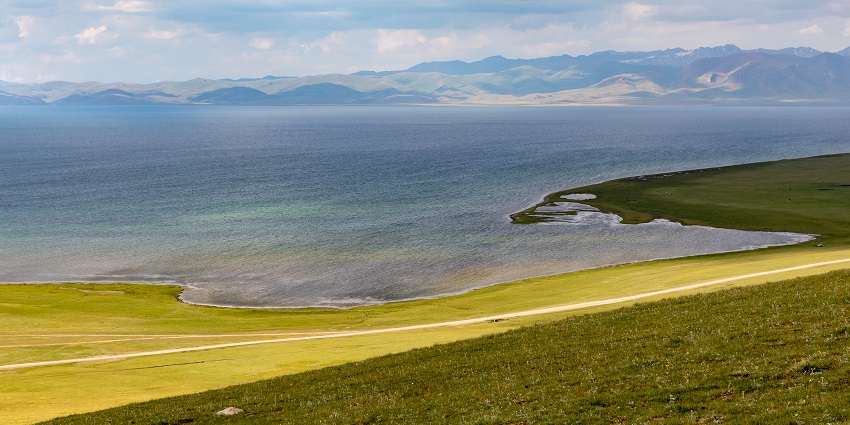 A serene alpine lake surrounded by rolling hills and nomadic yurts during the daytime.