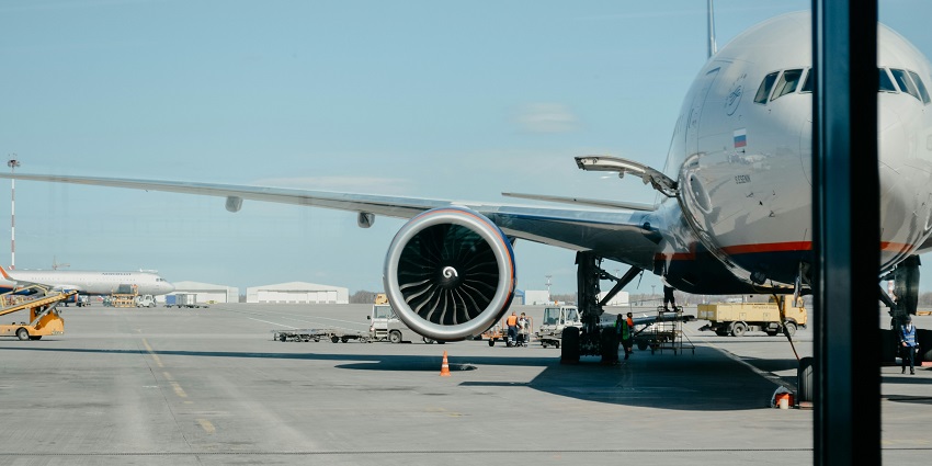 A large airplane parked at the airport gate with ground crew and vehicles nearby.