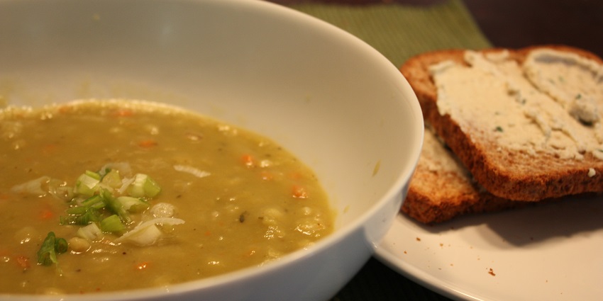 An image of a warm bowl of thick and creamy delicious split pea soup served with bread.