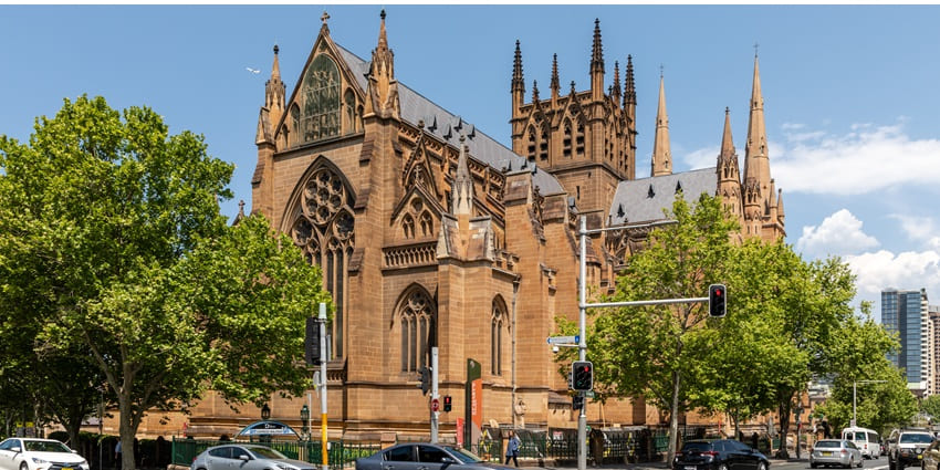 St. Mary's Cathedral in Sydney, Australia, with cars on the road and lush green trees around