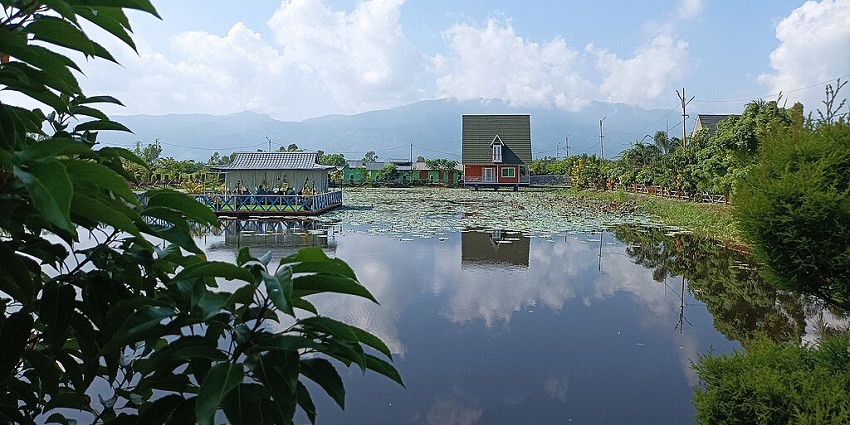Floating homestay in Manipur with houses and lily pads on the lake and greenery.