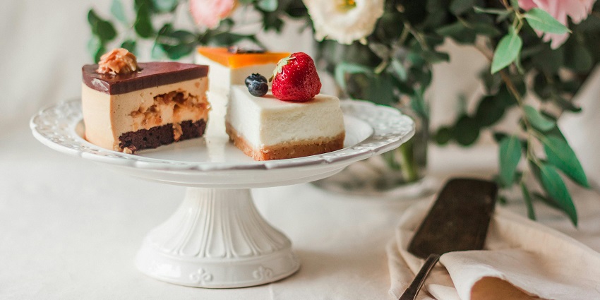 Two slices of different cheesecakes served on a white dish with a flower pot behind them