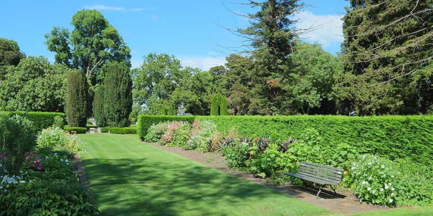 The Sunken Garden featuring symmetrical pathways, trimmed hedges, tall trees, and colourful flowers.