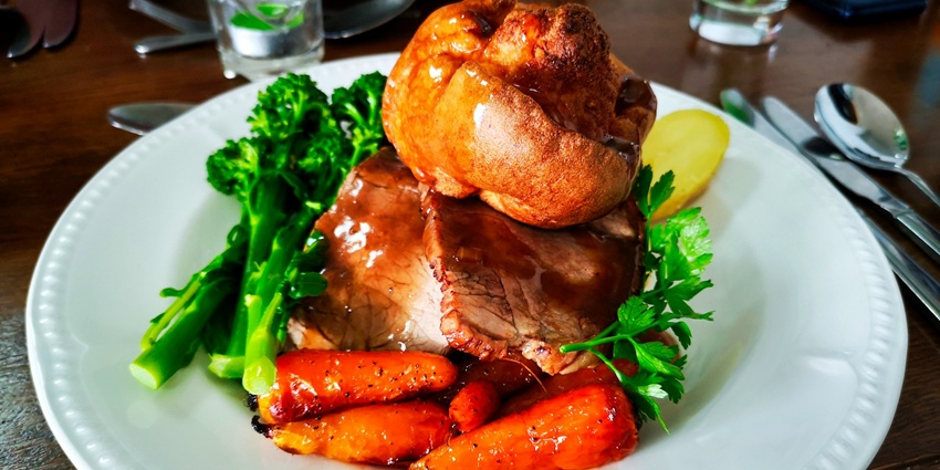 An image showing roasted chicken beside pudding on a glass tray and a bowl of fruits.