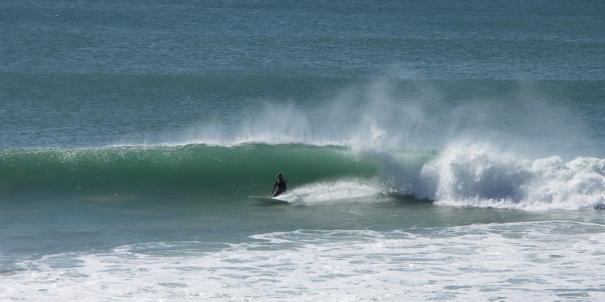 A surfer expertly riding a curling ocean wave, with rocky shoreline at the Jeffreys Bay.