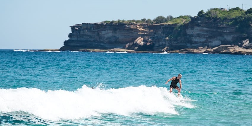 Man surfing over medium waves enjoying the water sport and cliffs in the background.
