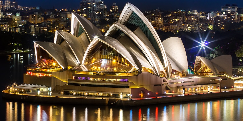 A photograph of the Sydney Opera House and its iconic sail-design building set amidst the harbour.