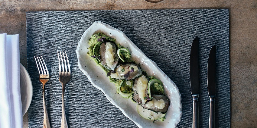 Rock oysters with vegetables, white sauces, forks and knife served on a designer plate