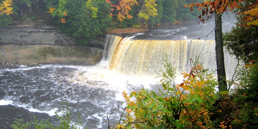 A scenic, tannin-coloured waterfall in Michigan, surrounded by densely forested landscapes.