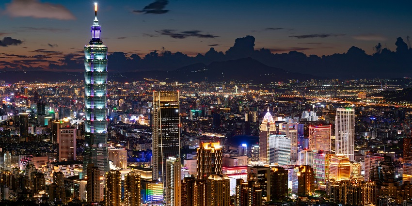 View the night skyline of Taipei City, Taiwan with illuminated skyscrapers, and vibrant city lights against a dark mountainous backdrop.