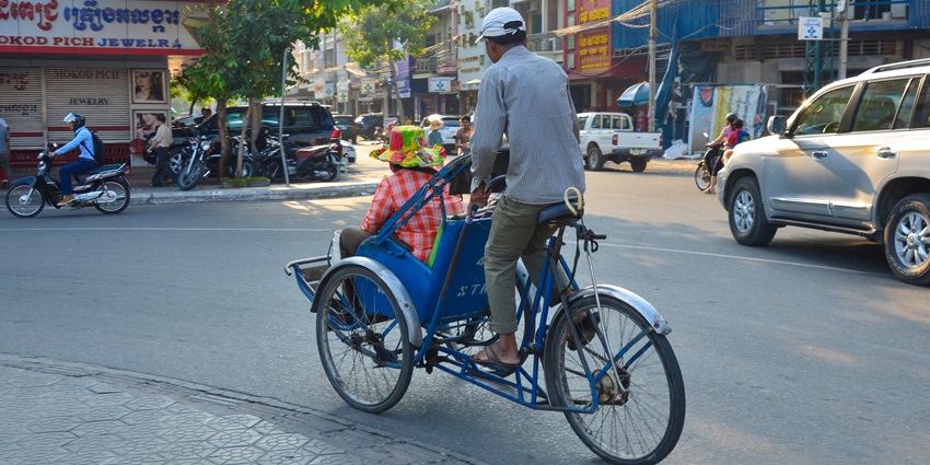 Tourists riding cyclos past French colonial buildings in central Phnom Penh city streets.