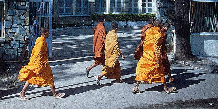 Six people in orange and brown traditional monk robes walking outside Phnom Penh.