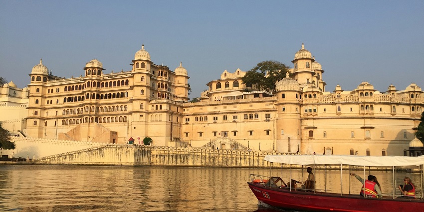 A boat with a large palace and waterway in the background, showcasing the boat ride in Udaipur.