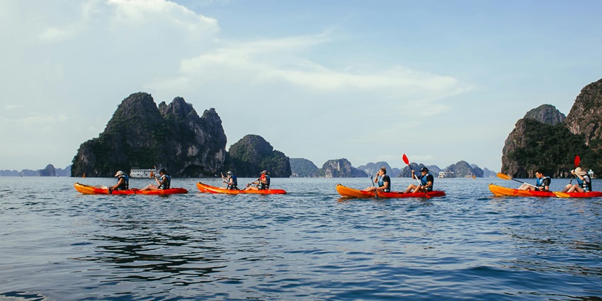 Two kayakers navigating calm waters surrounded by dramatic limestone cliffs.