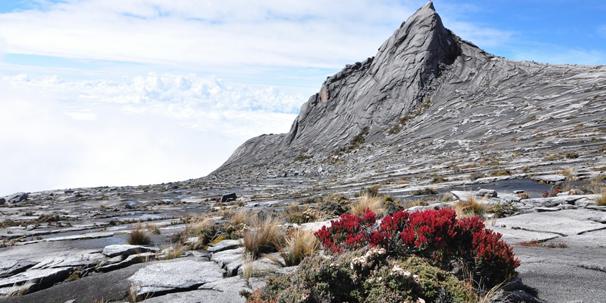 Majestic gray mountain under a clear blue sky with scattered white clouds.