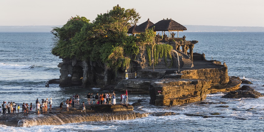 Tanah Lot Temple sits atop a rocky island, surrounded by ocean waves and visitors
