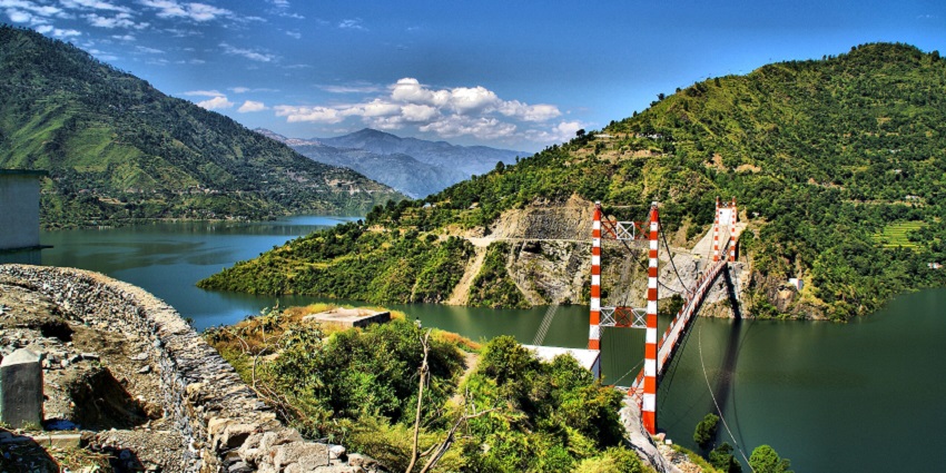 Tehri lake with a narrow iron bridge over a large water body surrounded by green mountains