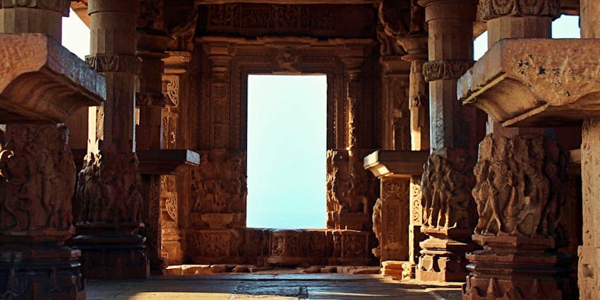 An interior view of a temple with carved stone pillars and an open doorway framing the sky
