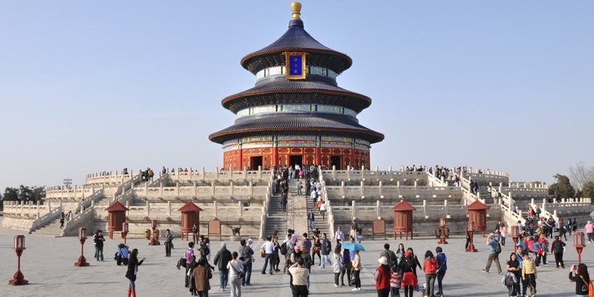 Visitors are walking towards the Temple of Heaven, which is standing under a clear sky.