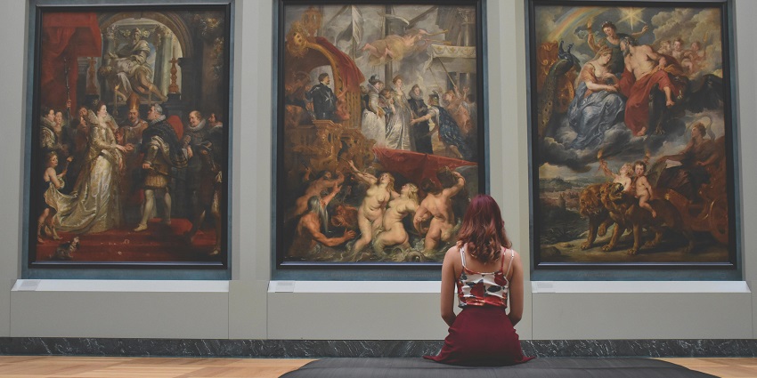 An image of a person seated on a bench, observing historical and mythological paintings, similar to the Avenue Gallery in Victoria.