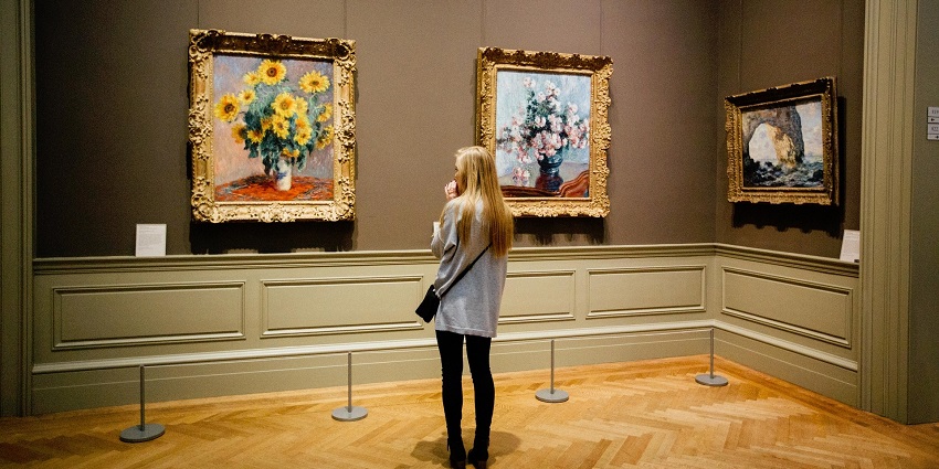 An image showing a woman admiring a painting of flowers, displayed at The National Gallery of Iceland