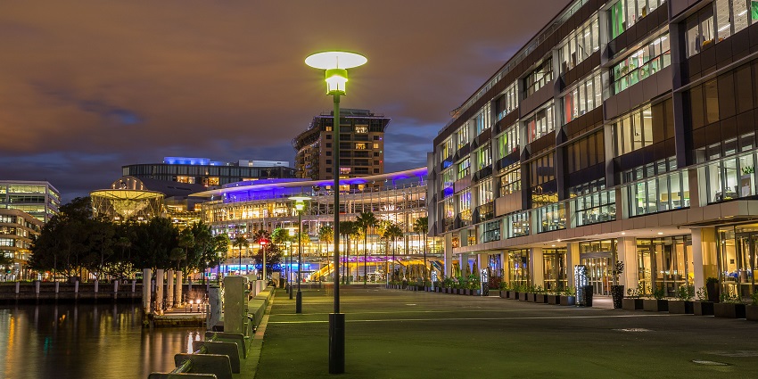 A waterfront cityscape is glowing with artificial lights, reflecting on the calm water at night.